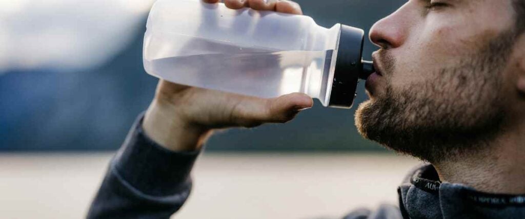 A close up of a male runner drinking out of his water bottle. 
