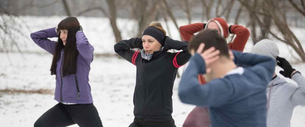 A group of runners stretching in the park with snow on the ground and bundled up in warm clothes. 