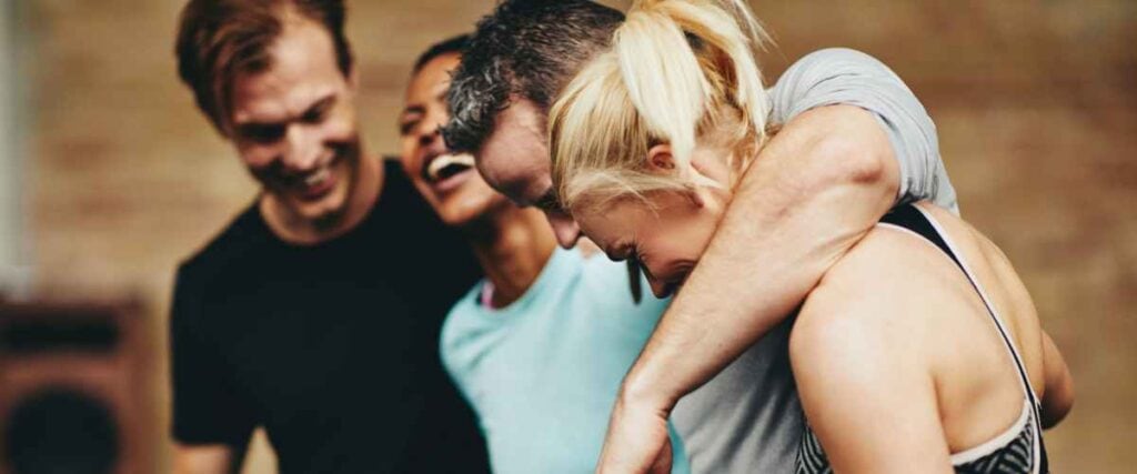 A group of friends with their arms around each other laughing at the gym. 
