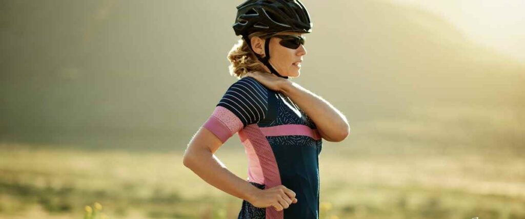 A female cyclists on the side of the road catching her breath holding her should looking ahead. 
