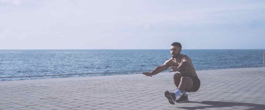 A man doing the pistol squats on the walkway next to the beach.