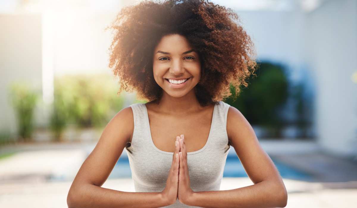 A woman holding her hands together with a big smile about to mediate before her workout. 