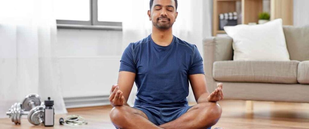 A man in his living room mediating before his workout. 