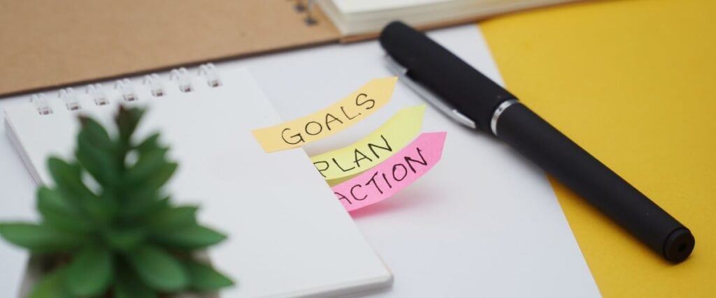 A pen and notebook with the words 'goals, plan, action' written on it. 