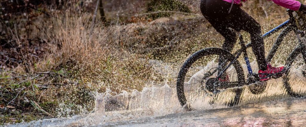 A female mountain biker going thru a big water puddle. 