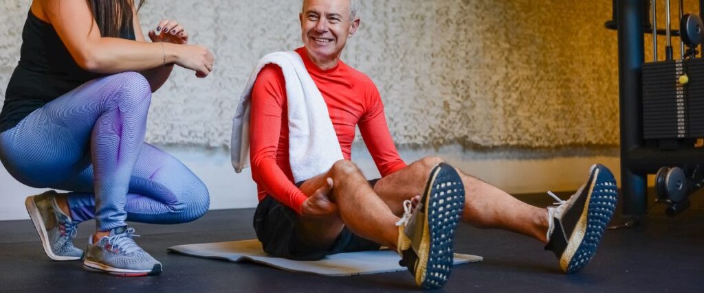 A man sitting on a yoga mat with his personal trainer. 