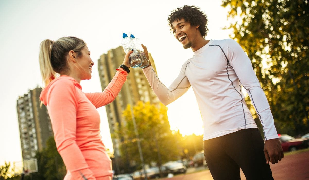 Two people cheering their water bottles after a workout. 