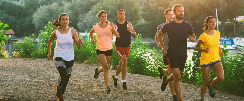A group of runners in a park next to a lake. 