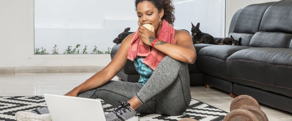 A woman eating an apple on her floor about to exercise. 