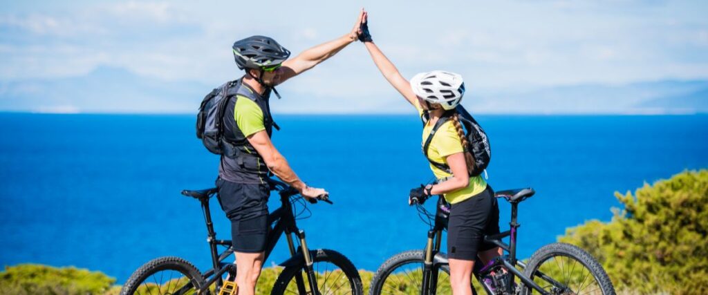 A couple on their bike high-fiving looking over a lake. 