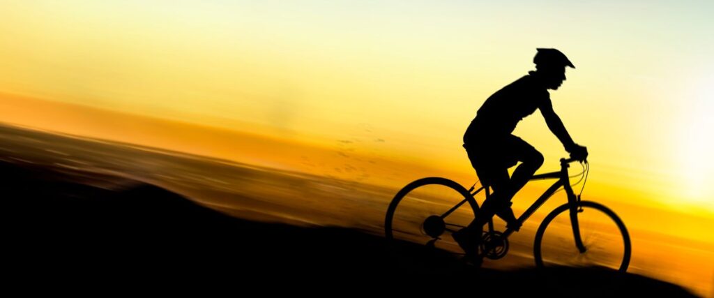 A cyclists going down hill during the sunset. 