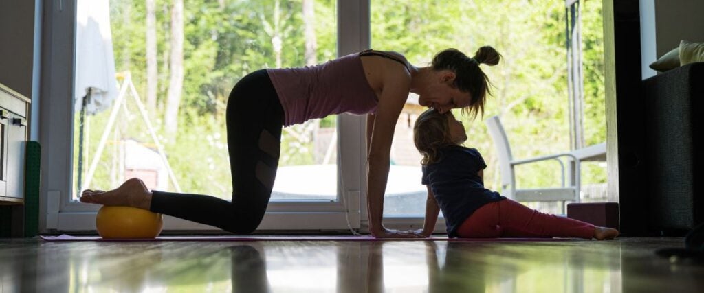 A mom doing yoga poses at her house with her daughter trying to play with her while working out. 
