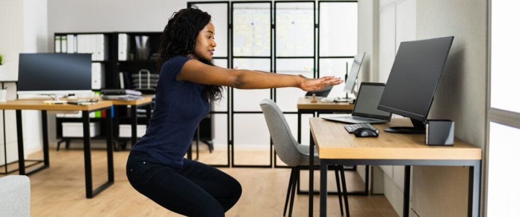 A woman doing lunges at her work desk. 