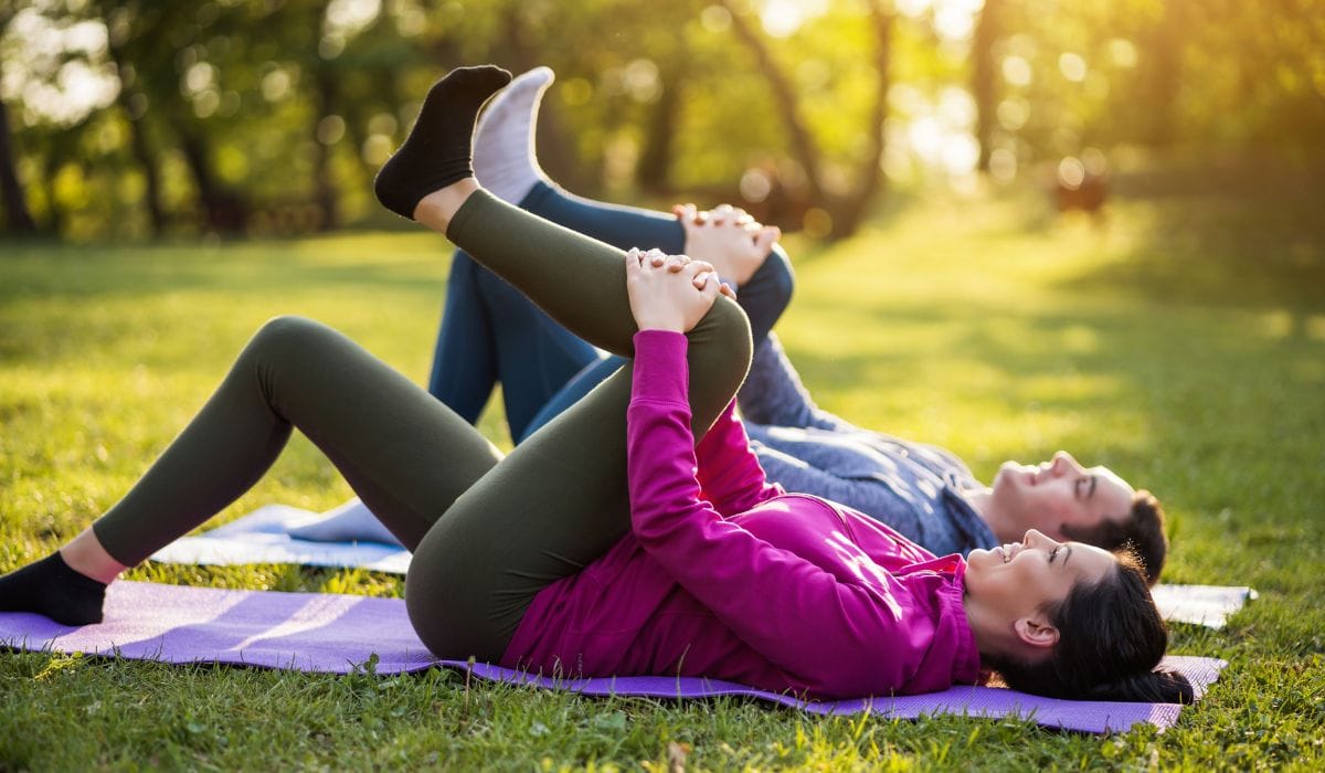 A couple stretching on yoga mat in a park. 