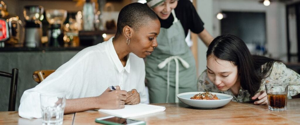 Two women at a dinner table smelling the food from the chef.