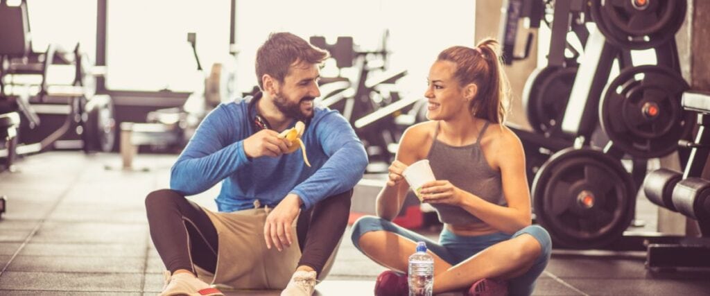 A couple at the gym eatting healthy food on the gym floor. 