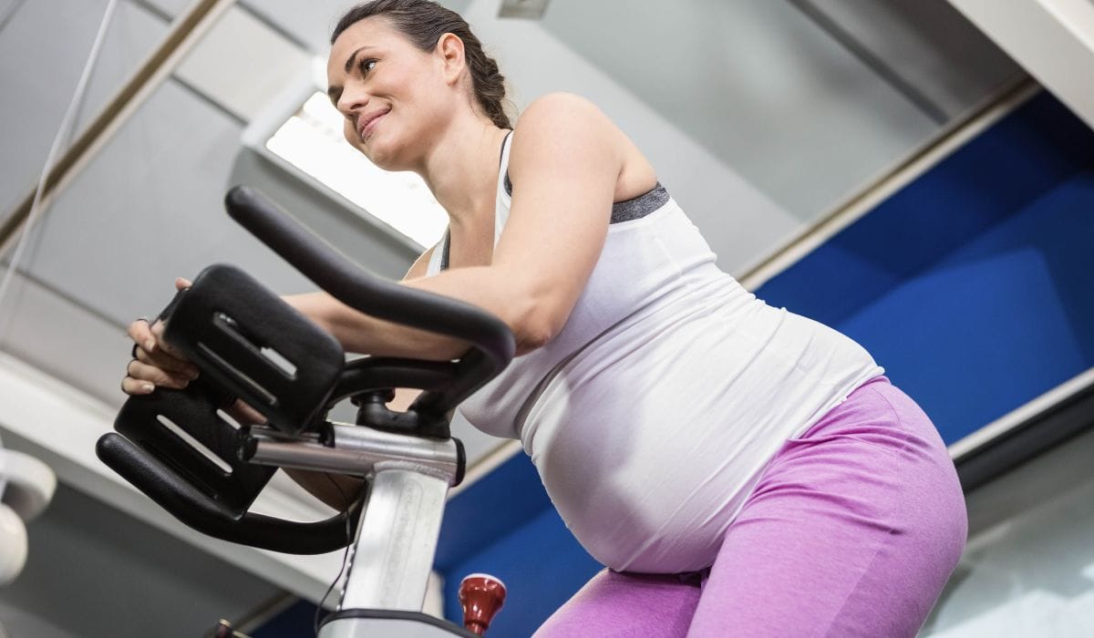A pregnant women on a stationary bike at the gym. 