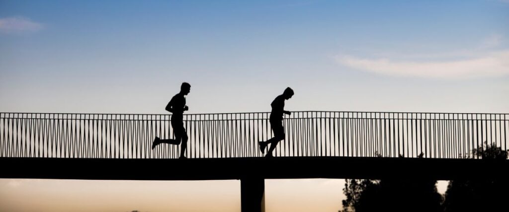 Two runners on a bridge during the sunset. 