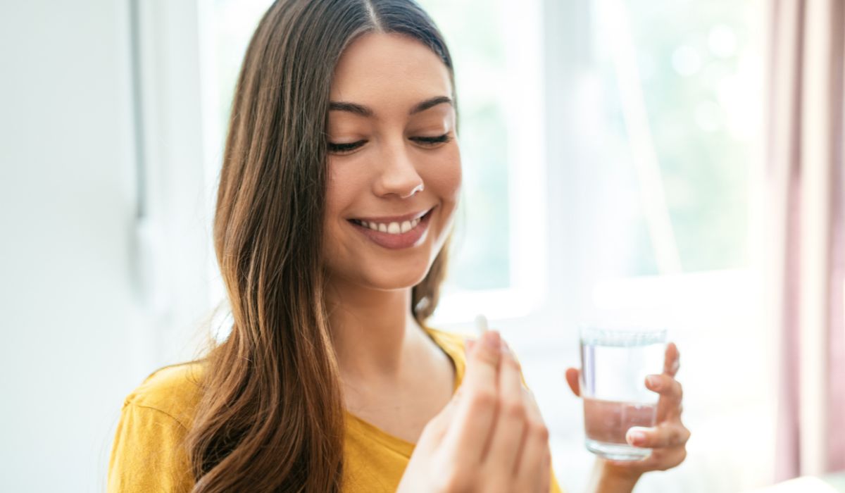 Women about to take a diet supplement with water looking down at her glass of water. 