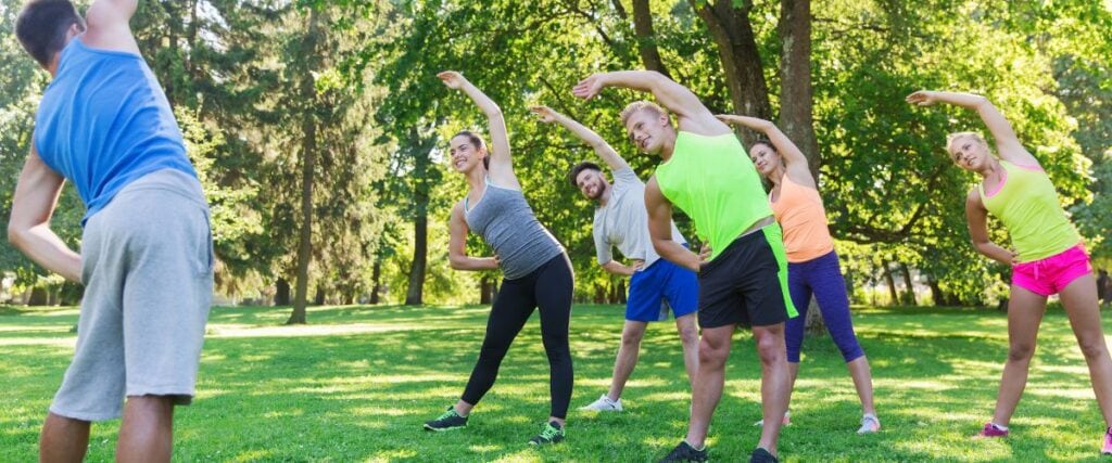 A group of people at a park stretching before a group workout. 
