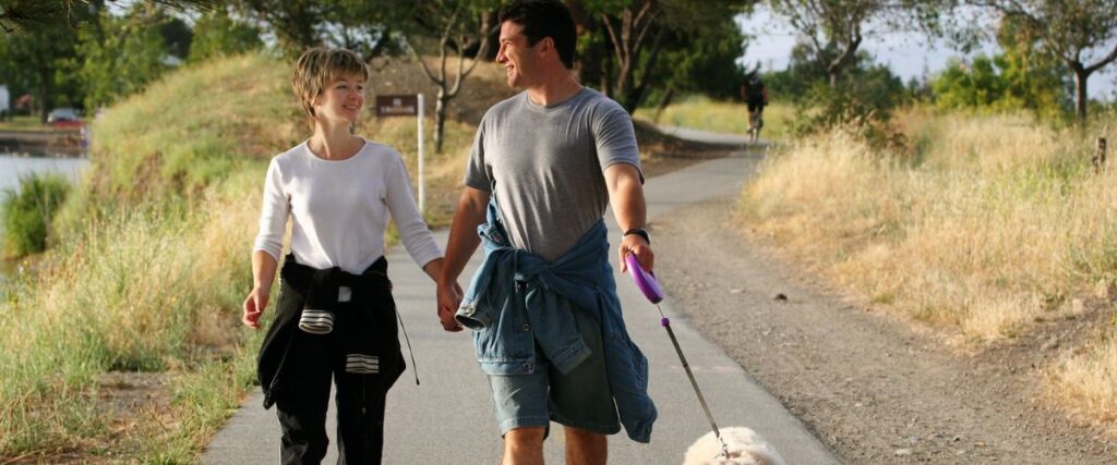 A couple holding hands while walking their dog in a park. 
