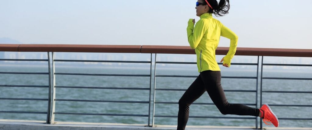 A female runner on the beach next to the fence. 