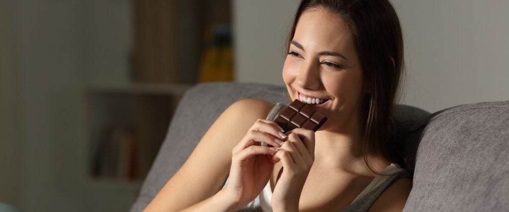 A woman eating dark chocolates on her couch at home. 