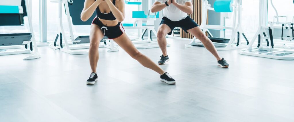 A couple doing side-lunges at a gym together.