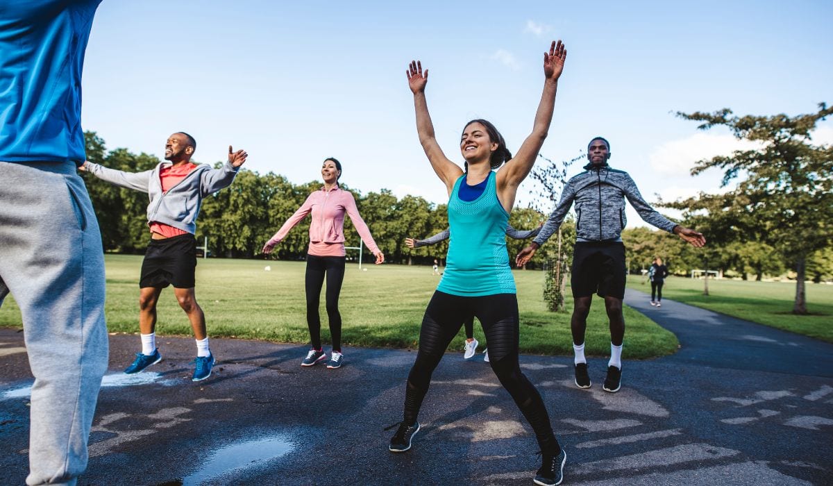 A group of people dong jumping jacks at a park together. 