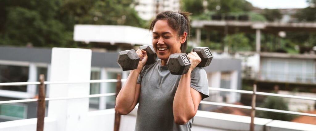 A woman holding 20lb weights on her root top gym. 