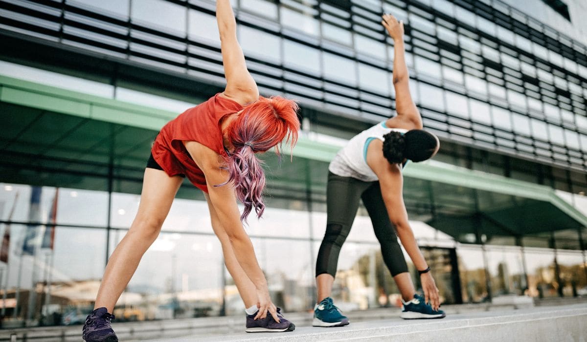 Two women stretching in front of a building after their workout. 
