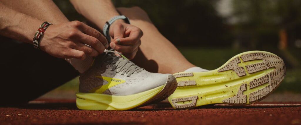 A runner taking a break and sitting on the ground to tie his sneakers.