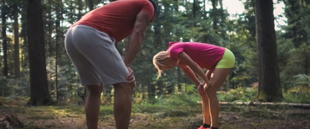 Two runners bending over after their run in the woods. 